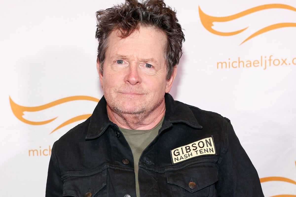 Michael J. Fox smiling at event, wearing dark suit and blue tie