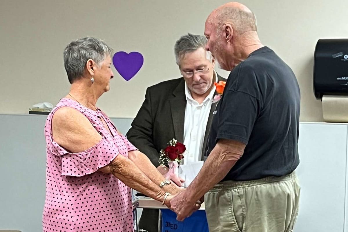 Couple renewing wedding vows in hospital room surrounded by caring nursing staff and flowers