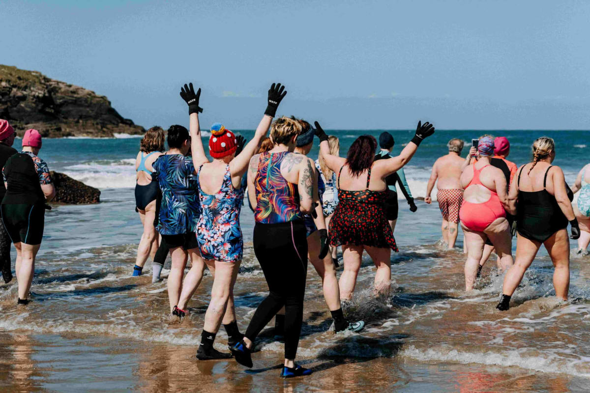 Group of people in colorful swimming caps gathering together by cold water, smiling and supporting each other