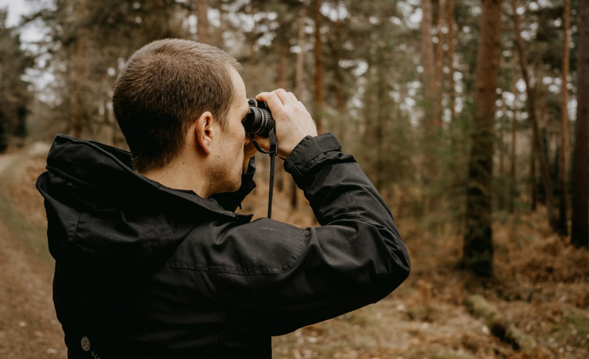 Young person with binoculars birdwatching at sunrise near water with trees