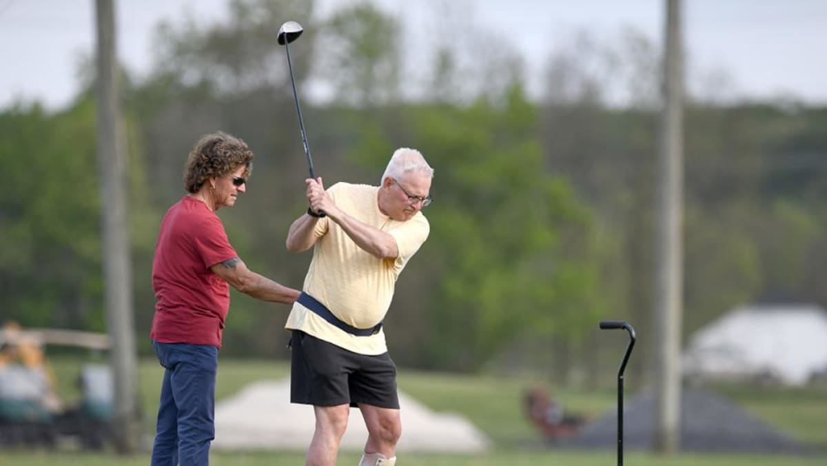 Jeffrey Rajchel practicing golf swing with friend's assistance after stroke recovery