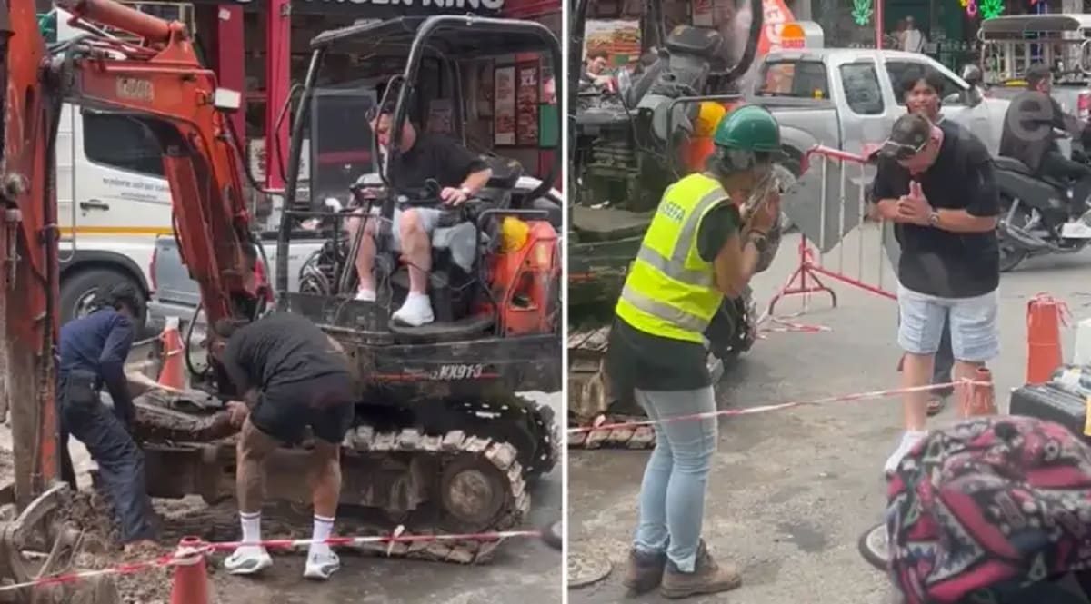 Australian tourists working alongside Thai construction crew to repair large yellow excavator track