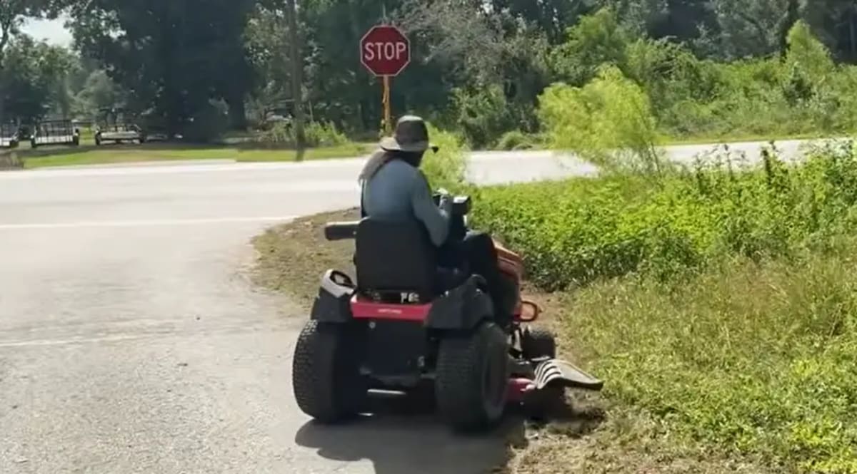 Man mowing tall grass around bus stop to create safe waiting area for children