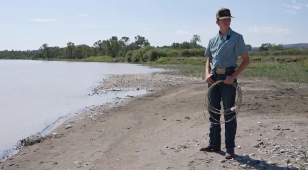 Teen cowboy Jory Thomas holding a lariat rope while standing near Montana riverbank