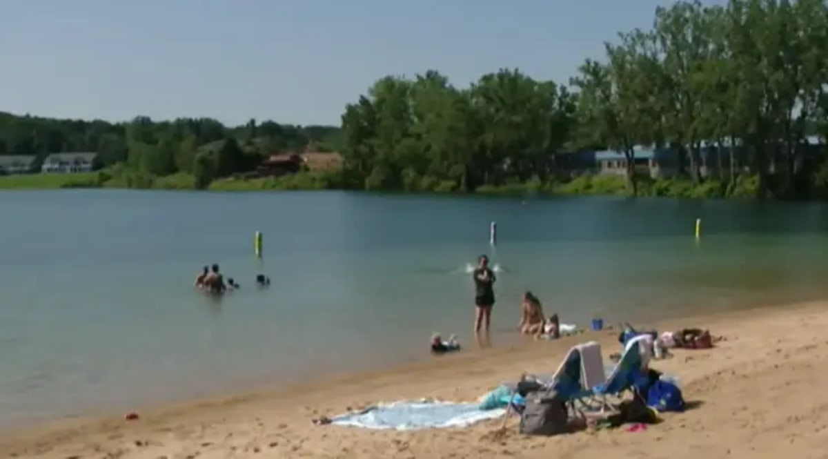 Woman performs CPR on young child at beach while emergency responders arrive at scene