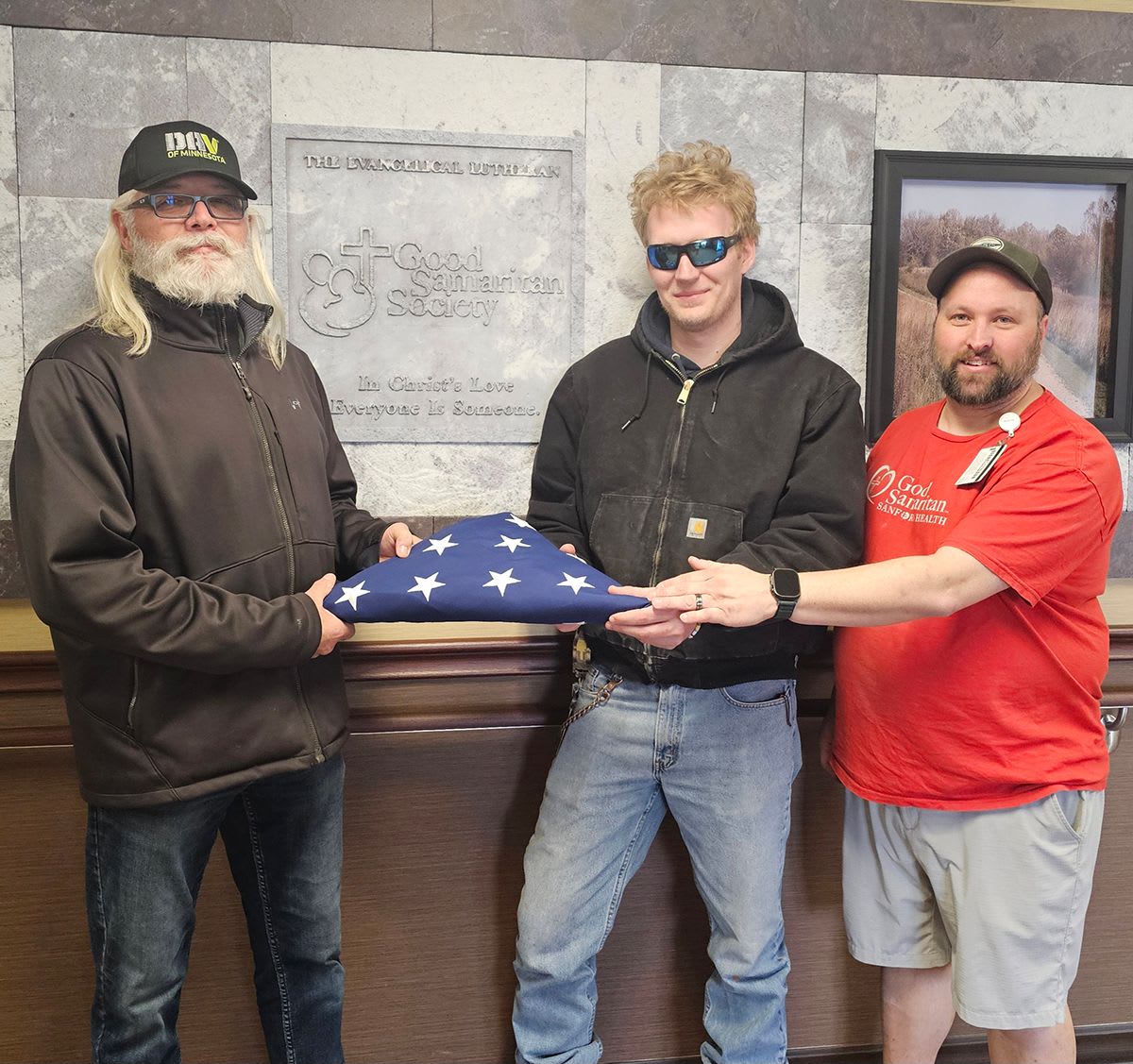 ** Dana Nelson presenting folded American flag to two Good Samaritan Society staff members