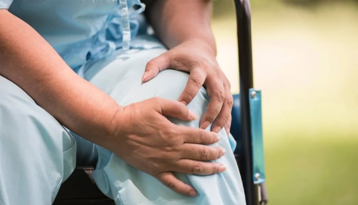 Person holding knee with one hand and fiber supplement bottle in other hand