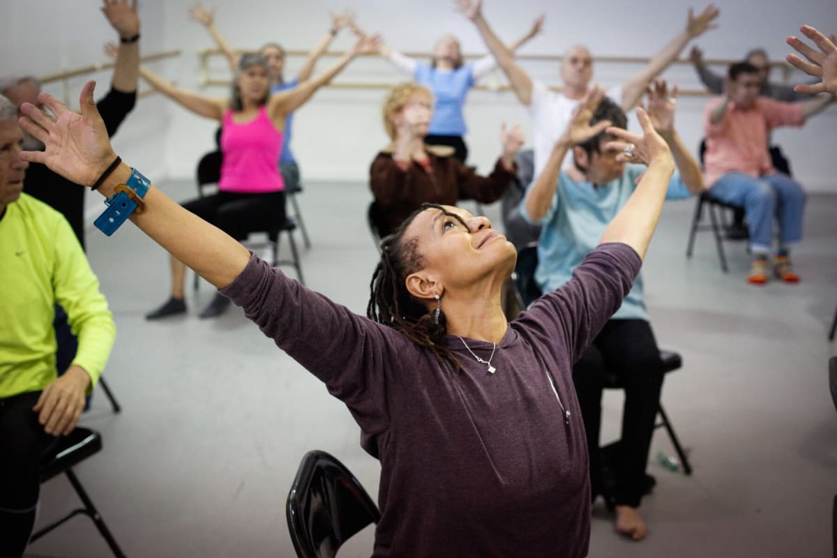 ** Group of people in chairs raising arms during Dance for PD therapeutic movement class