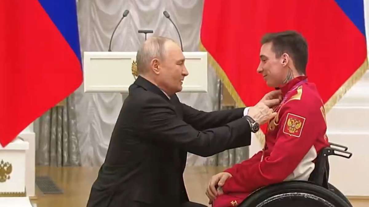 President Vladimir Putin kneeling while presenting award to Paralympic skiing champion Ivan Golubkov