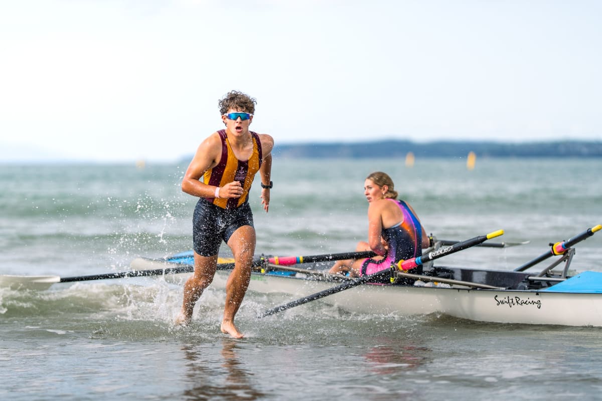 Two teenage rowers celebrating with gold medals on Orewa Beach after winning national championship