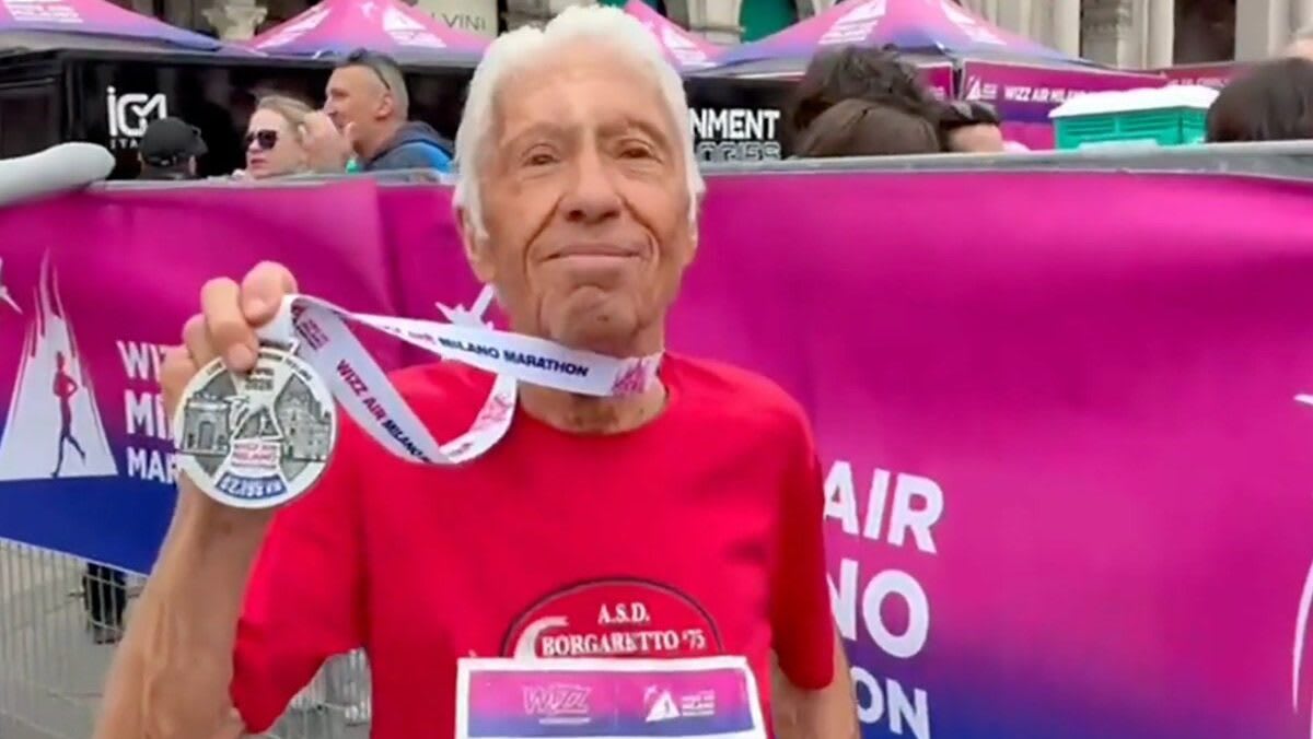 90-year-old Giuseppe Damato crossing finish line at Milan Marathon with pacers beside him