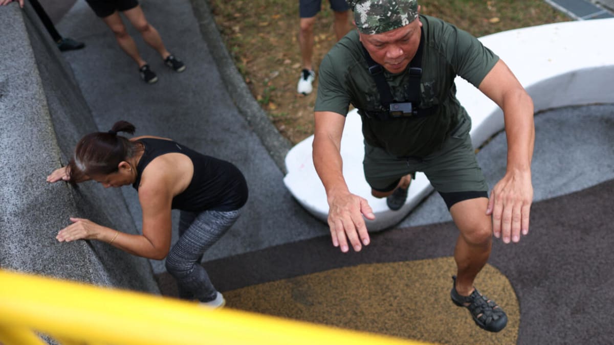 Senior adults in Singapore practicing parkour moves on outdoor structures during fitness class