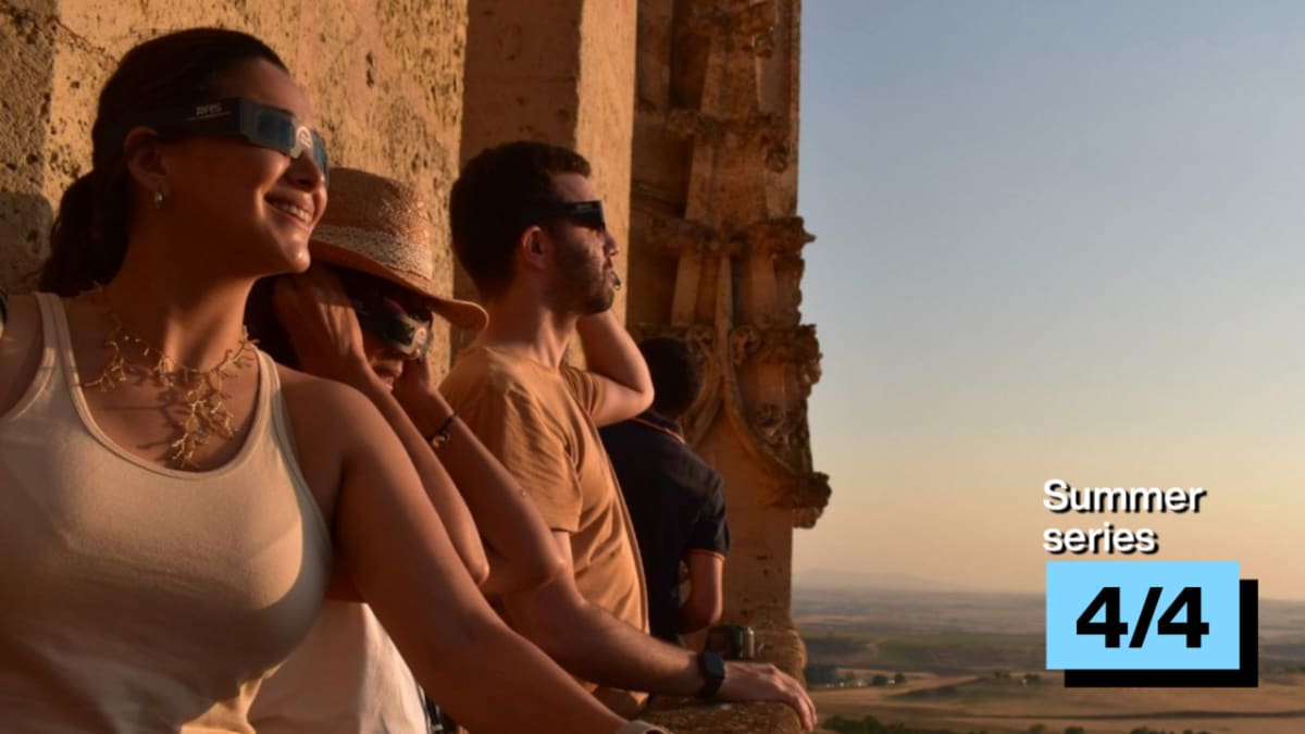 People wearing eclipse glasses observing total solar eclipse from historic Segovia cathedral bell tower in Spain