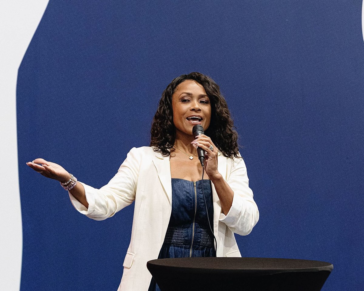 Dominique Dawes smiling in front of her youth gymnastics academy logo and facility