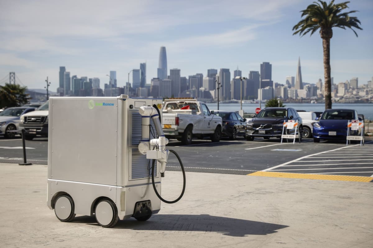 Refrigerator-sized autonomous robot with extended mechanical arm charging parked electric vehicle