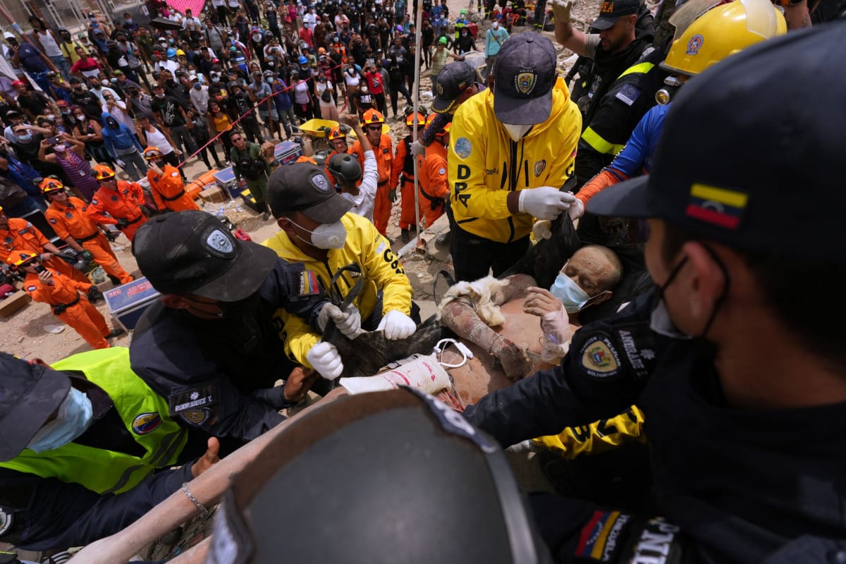 Rescue workers in hard hats carefully carry earthquake survivor on stretcher in Venezuela