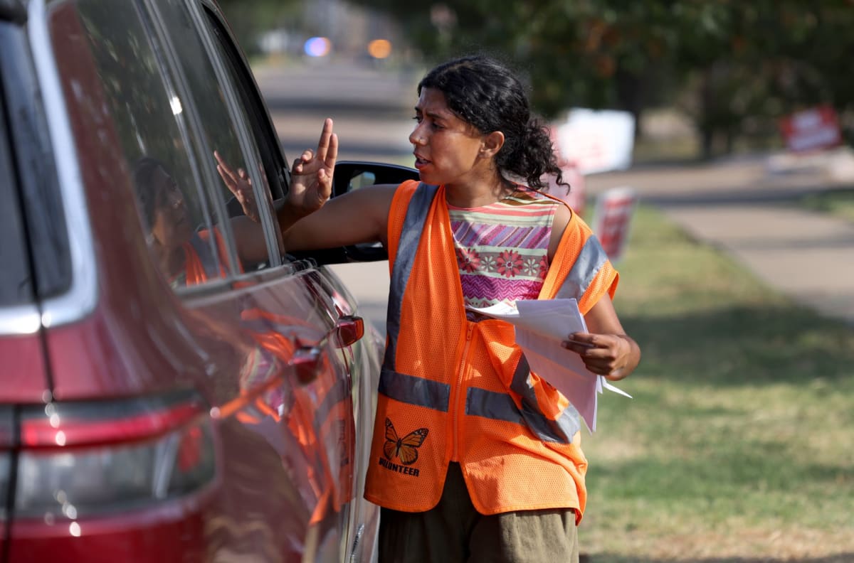 Volunteer in orange vest with butterfly symbol helps families outside Dallas ICE building