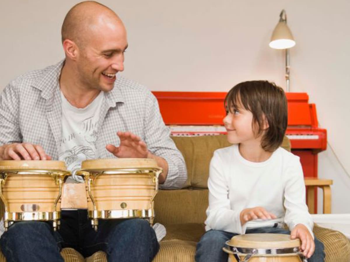 Ten children sitting at drum kits in circle while enthusiastic teacher conducts energetic music lesson