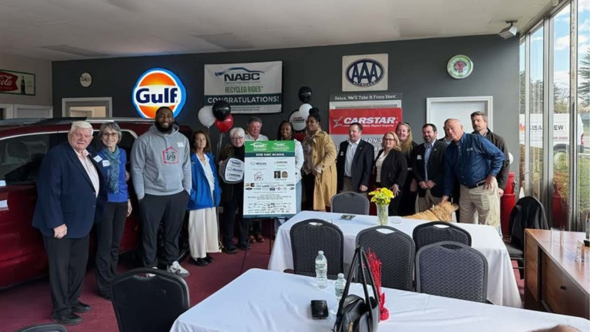 Red GMC Acadia SUV with charity representatives and auto body shop staff gathered for donation ceremony