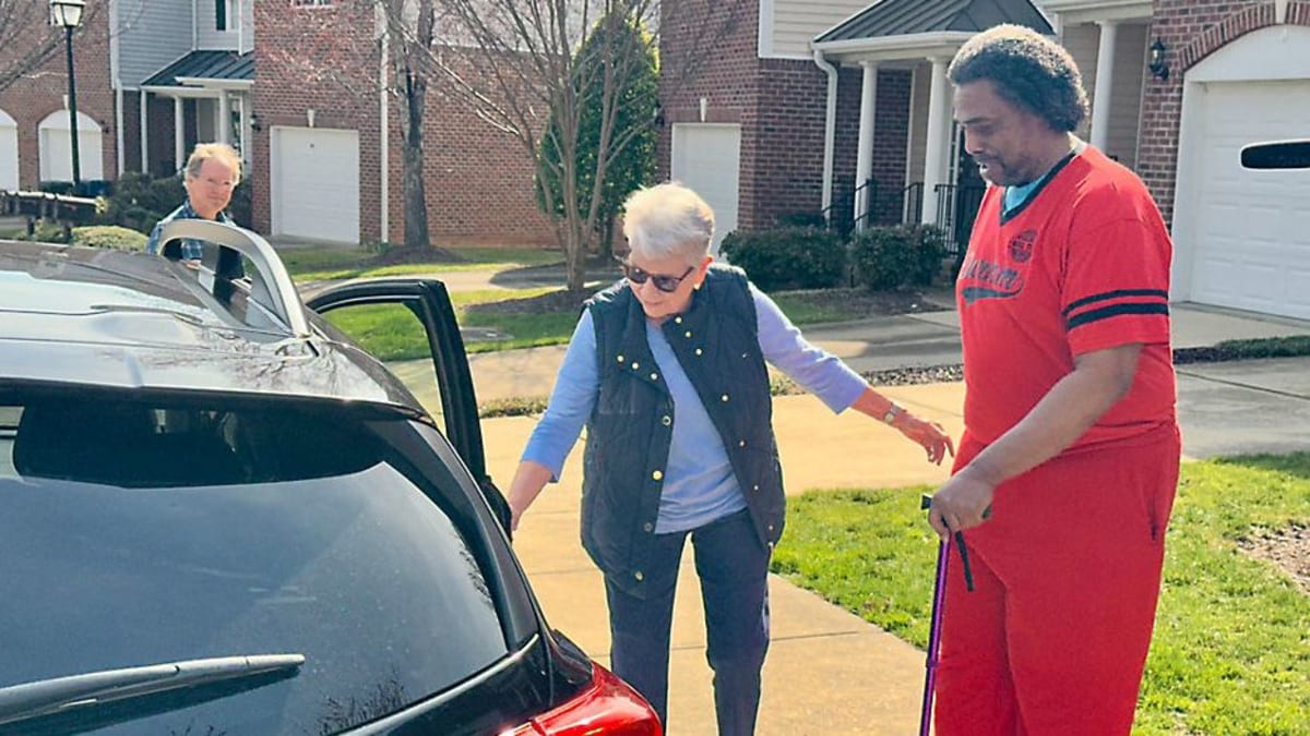 Volunteer driver Debby Leonard helping senior passenger Aaron Turrentine into car for medical appointment