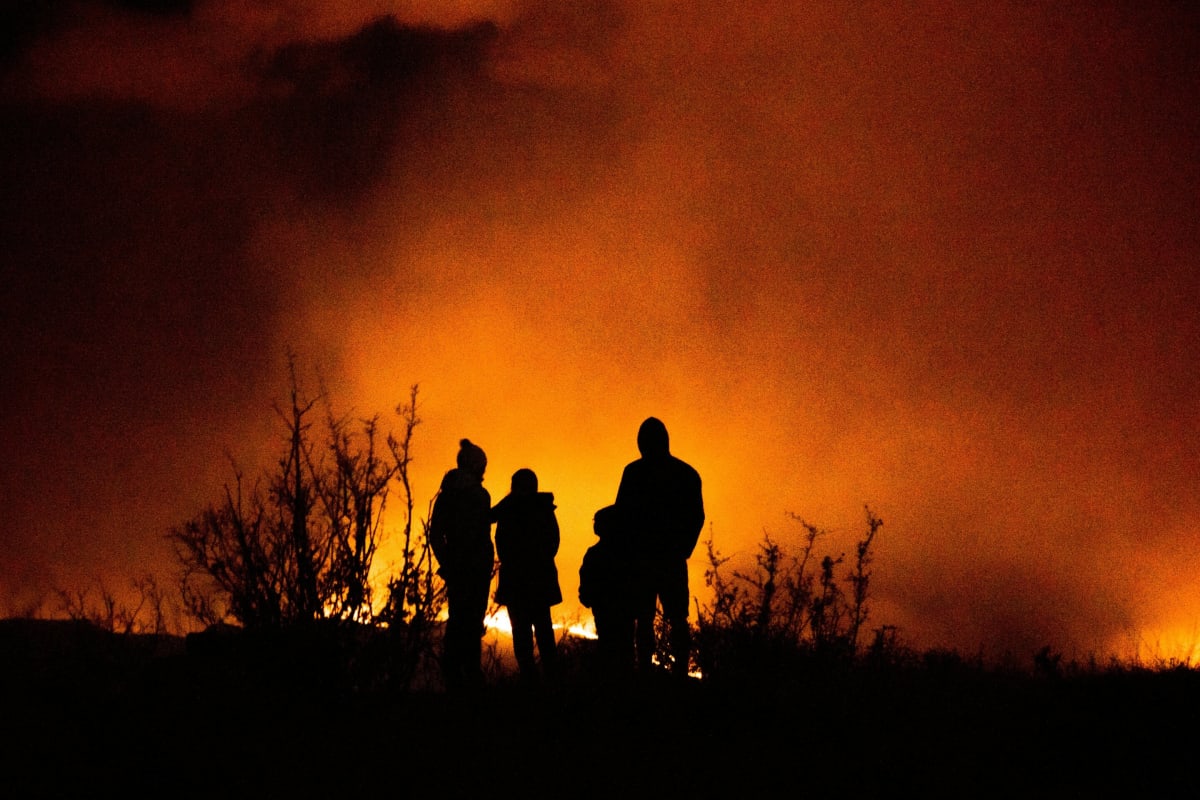 Wildfire spreading across landscape with smoke billowing into sky at sunset