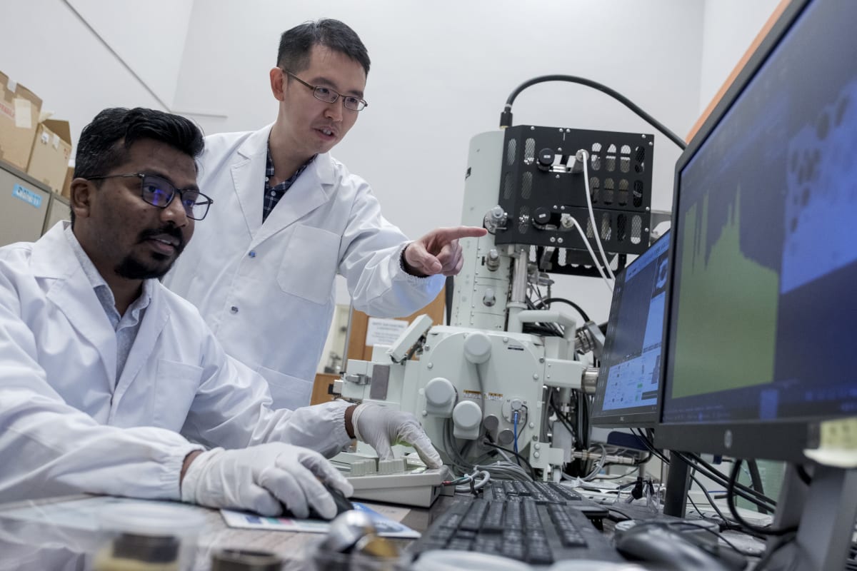 Two scientists in lab coats preparing graphite sample for X-ray experiment at microscope