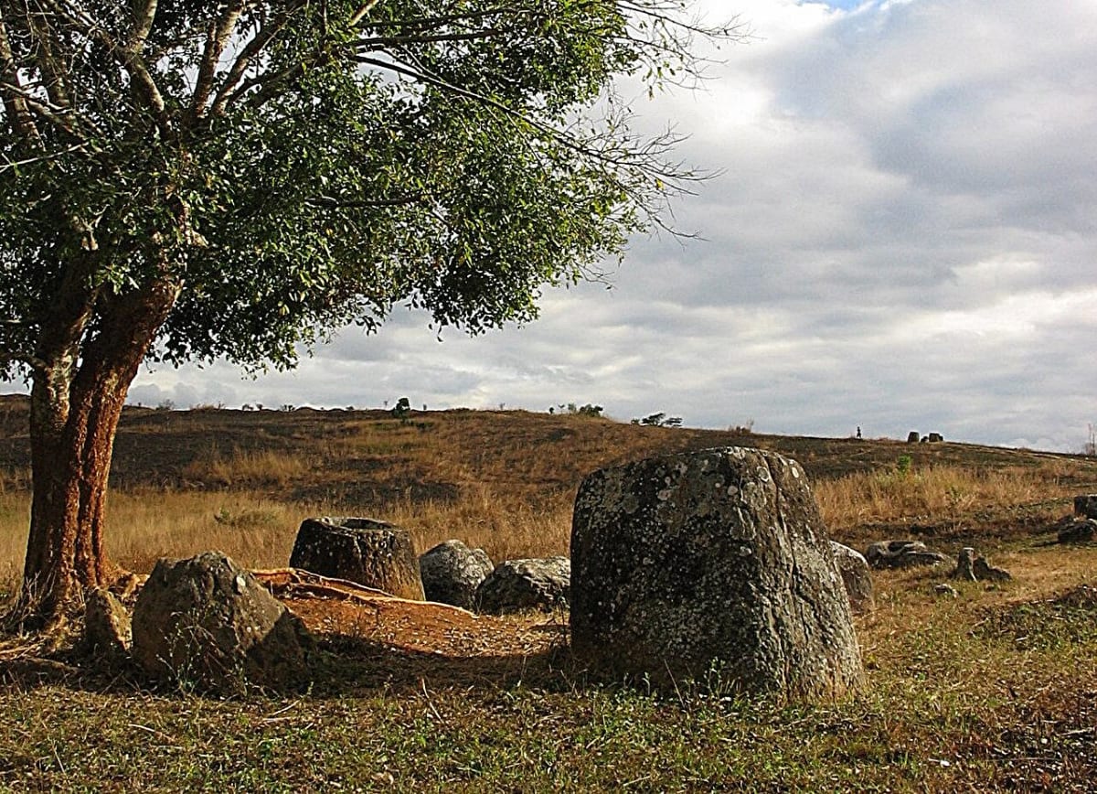 Ancient carved stone jars standing on grassy plain in Laos under blue sky
