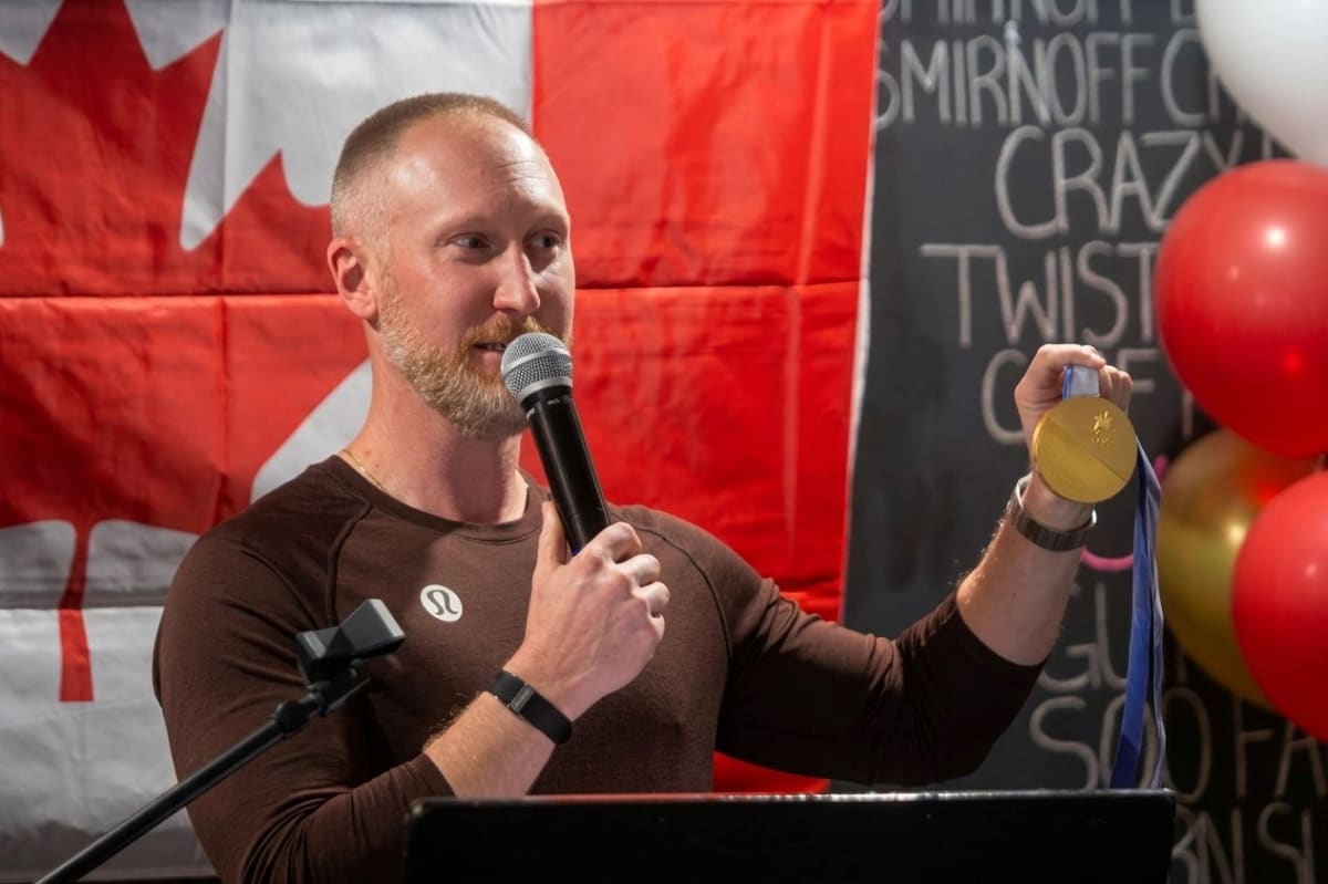 Brad Jacobs holding two Olympic gold medals at podium in Sault Ste Marie curling club