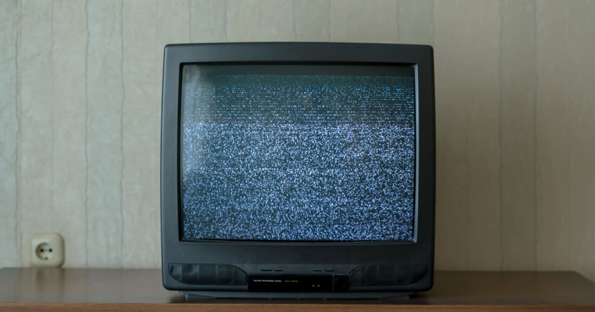 Vintage analog television displaying black and white static snow on screen in dark room