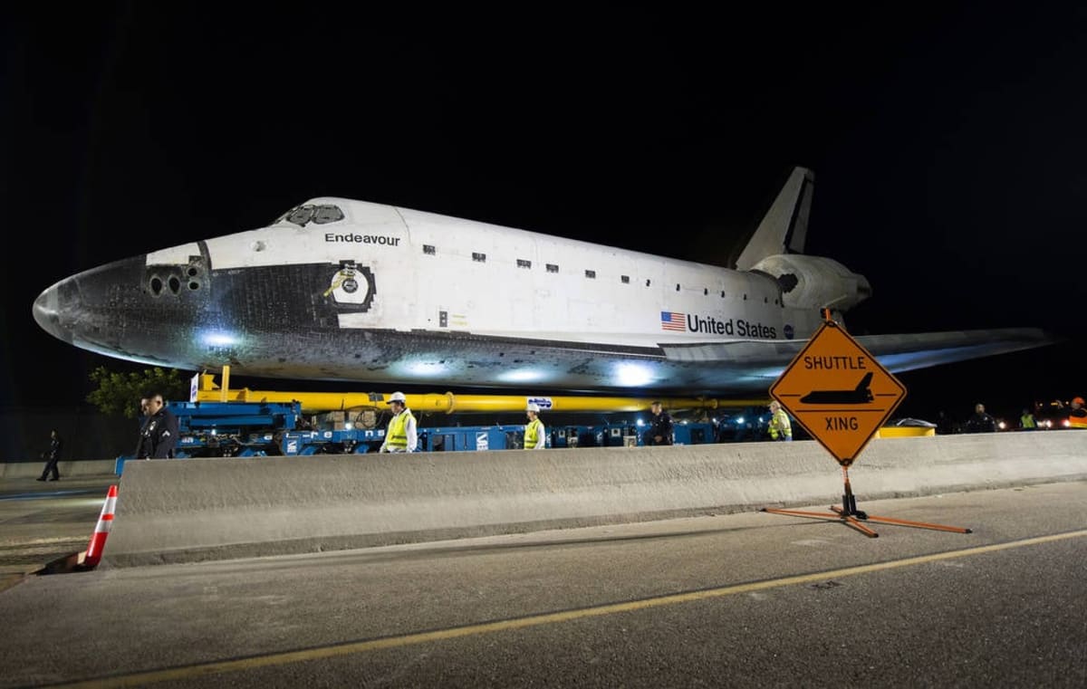 Space shuttle Endeavour on street transporter passing through Los Angeles neighborhoods with crowds watching