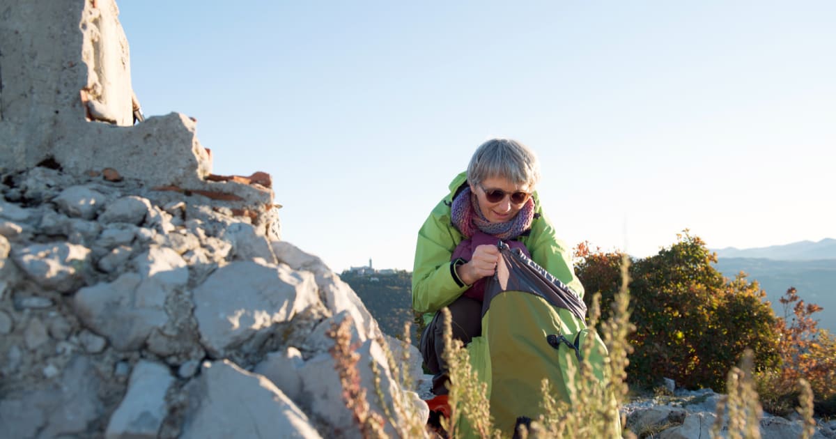 Elderly woman in simple hiking clothes walking mountain trail with homemade pack