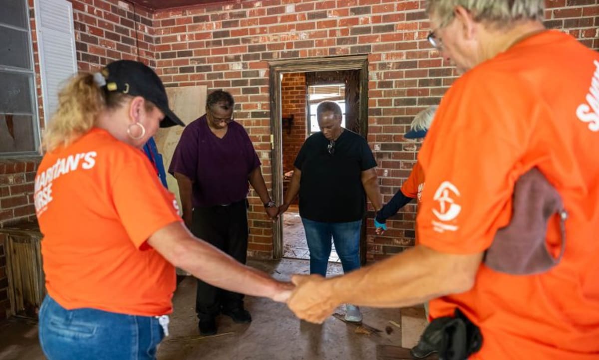 ** Volunteers in orange shirts helping remove water-damaged materials from Louisiana home after flooding