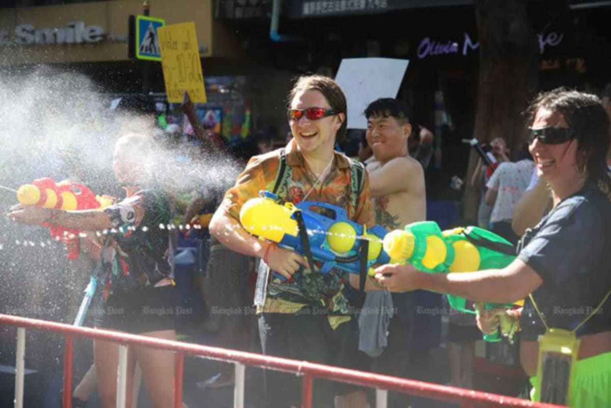 Smiling tourists and locals enjoying water fights during Songkran festival on Bangkok street
