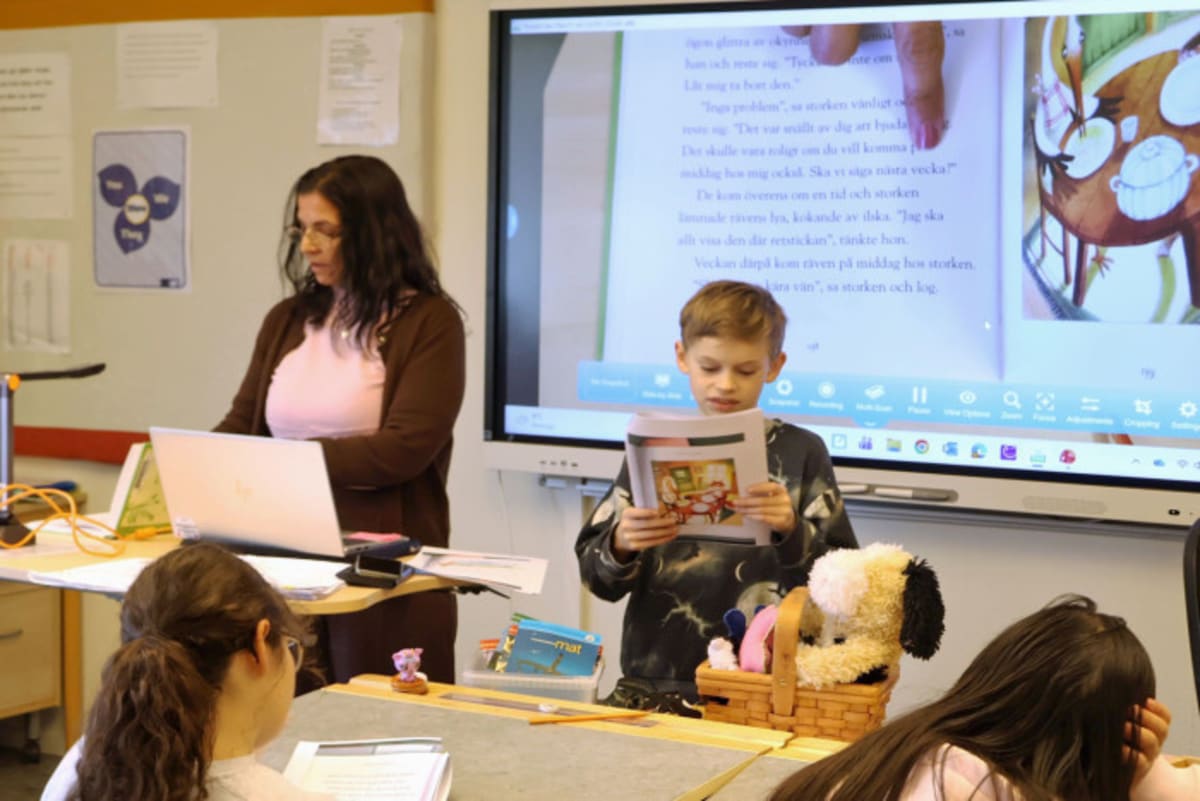 Swedish elementary student reading from printed textbook at desk in bright Stockholm classroom