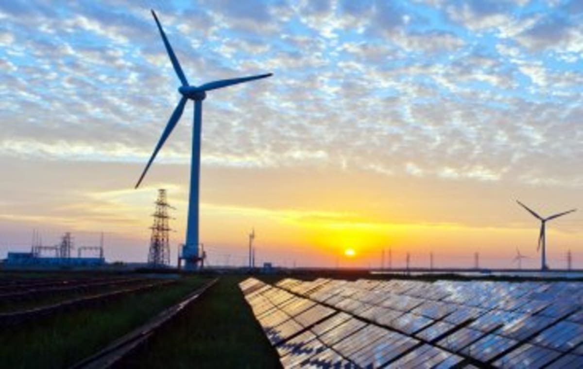 Solar panels stretching across Indian landscape with wind turbines in background under bright sky