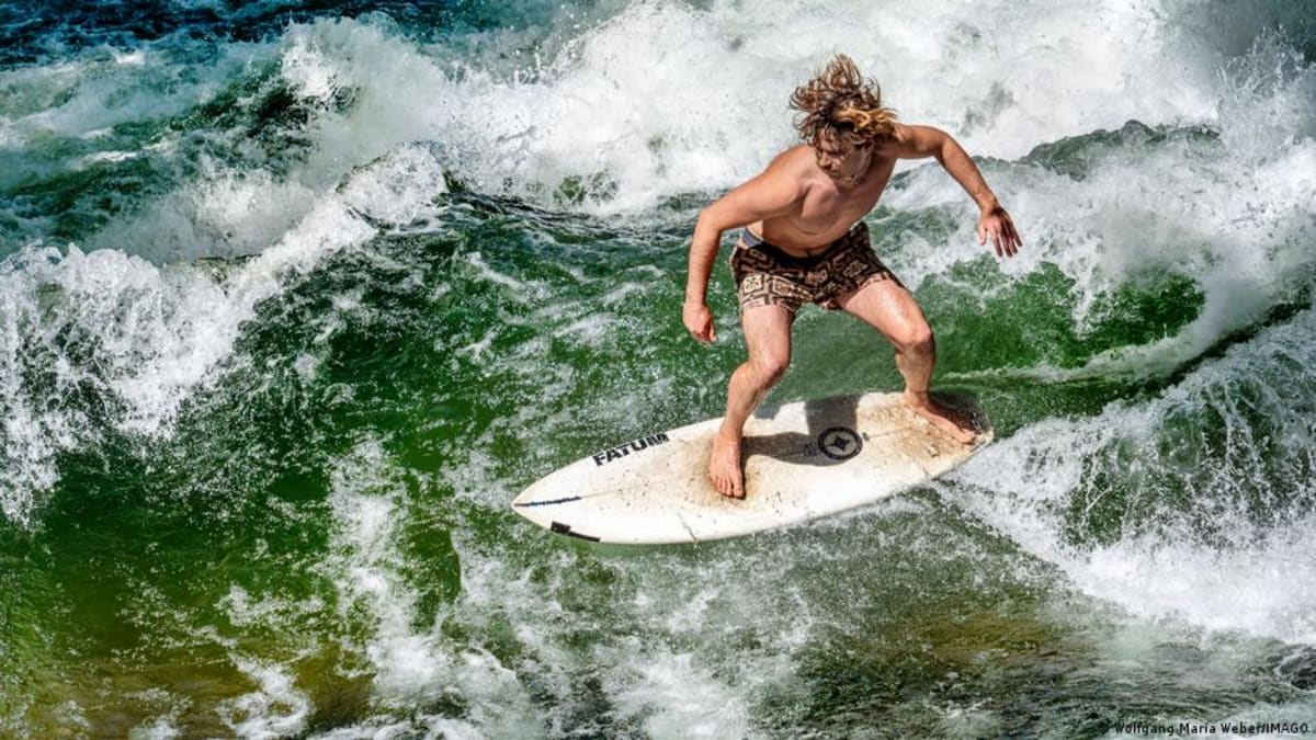 Surfer riding the Eisbach wave in Munich's English Garden with onlookers watching from bridge