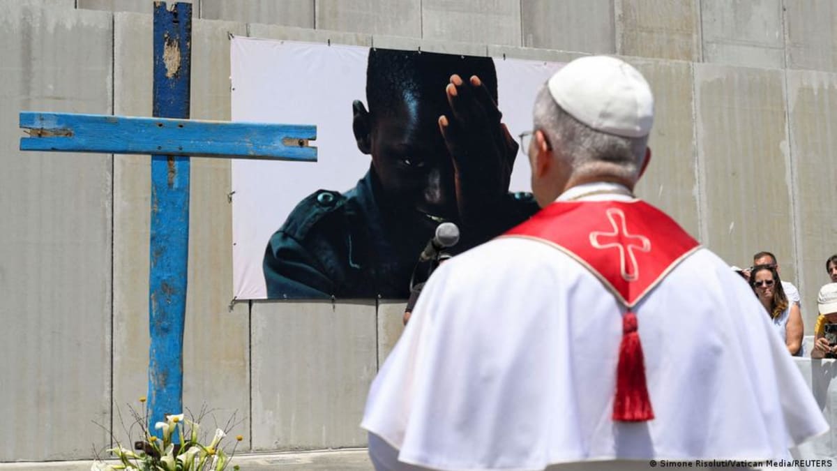 ** Pope Leo XIV standing at port beside wooden cross addressing gathered migrants