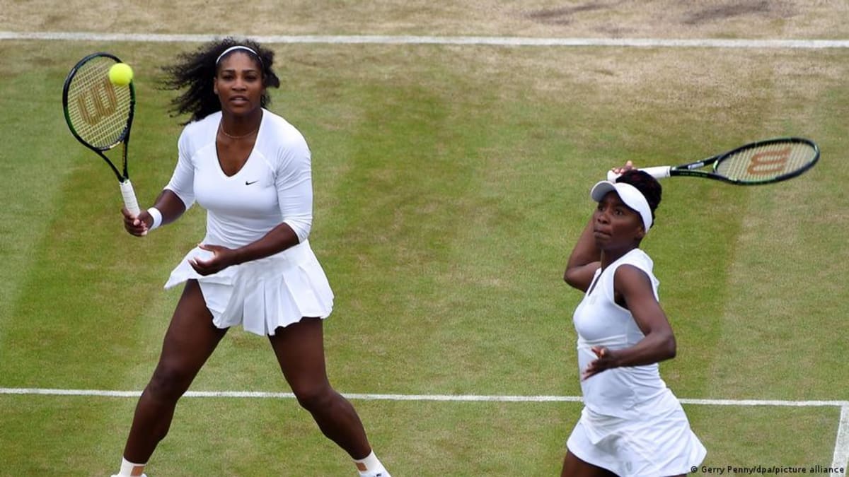 Serena and Venus Williams playing doubles tennis together on grass court