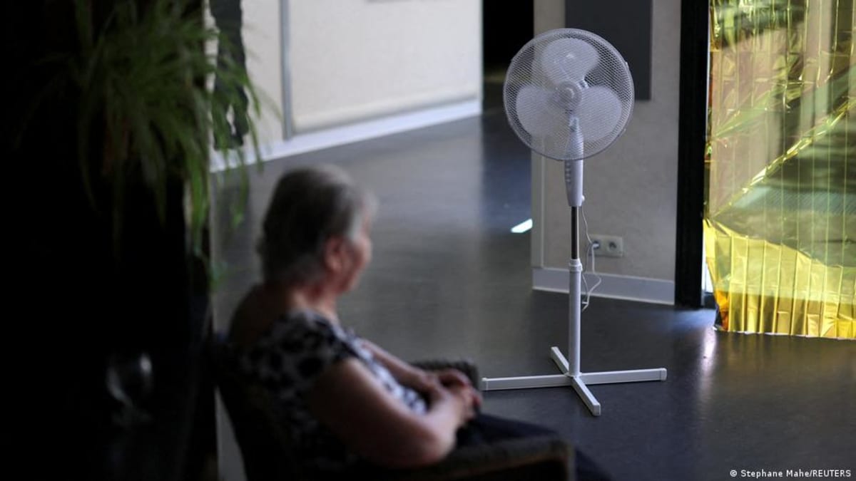 ** Person staying cool with electric fan during summer heat wave indoors