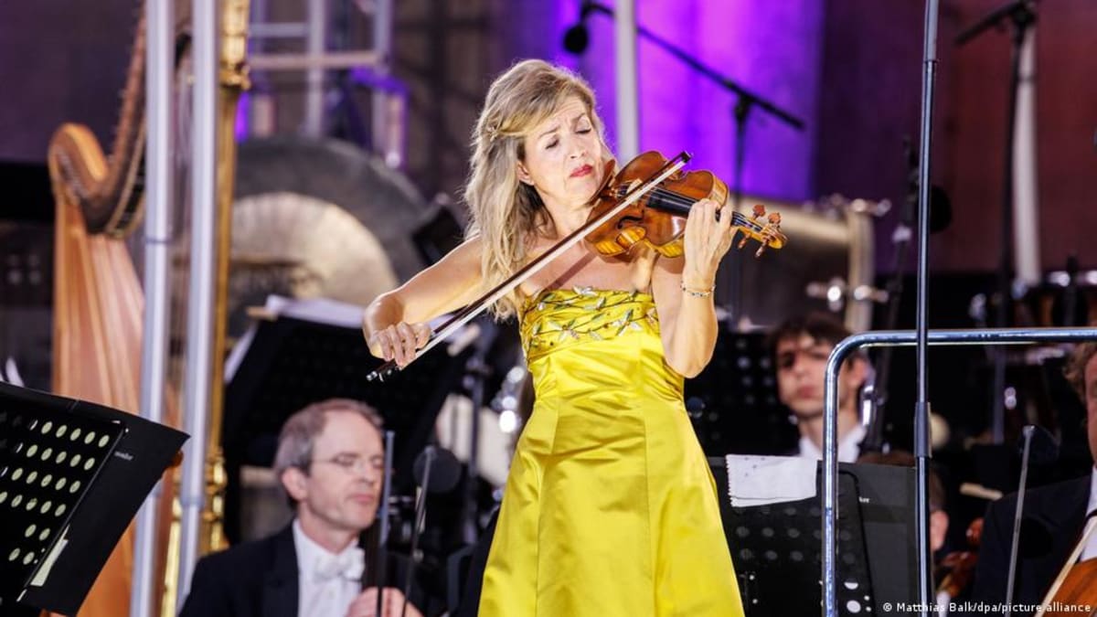 Star violinist Anne-Sophie Mutter performing with orchestra on world stage in elegant concert attire