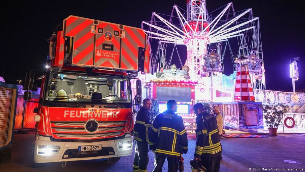 Firefighters with rescue ladders assisting passengers stranded on tall carnival swing ride in Hamburg