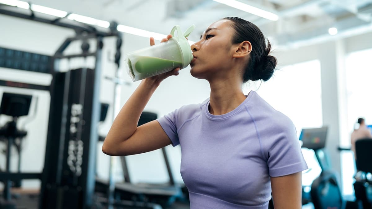 Person holding creatine supplement powder container next to water bottle in gym setting