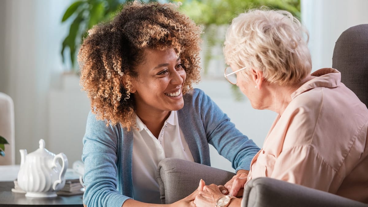 Senior woman smiling with family members gathered around her in warm, sunlit room