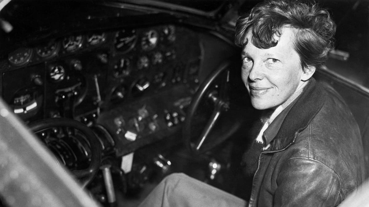 Black and white photograph of aviator Amelia Earhart standing beside her aircraft