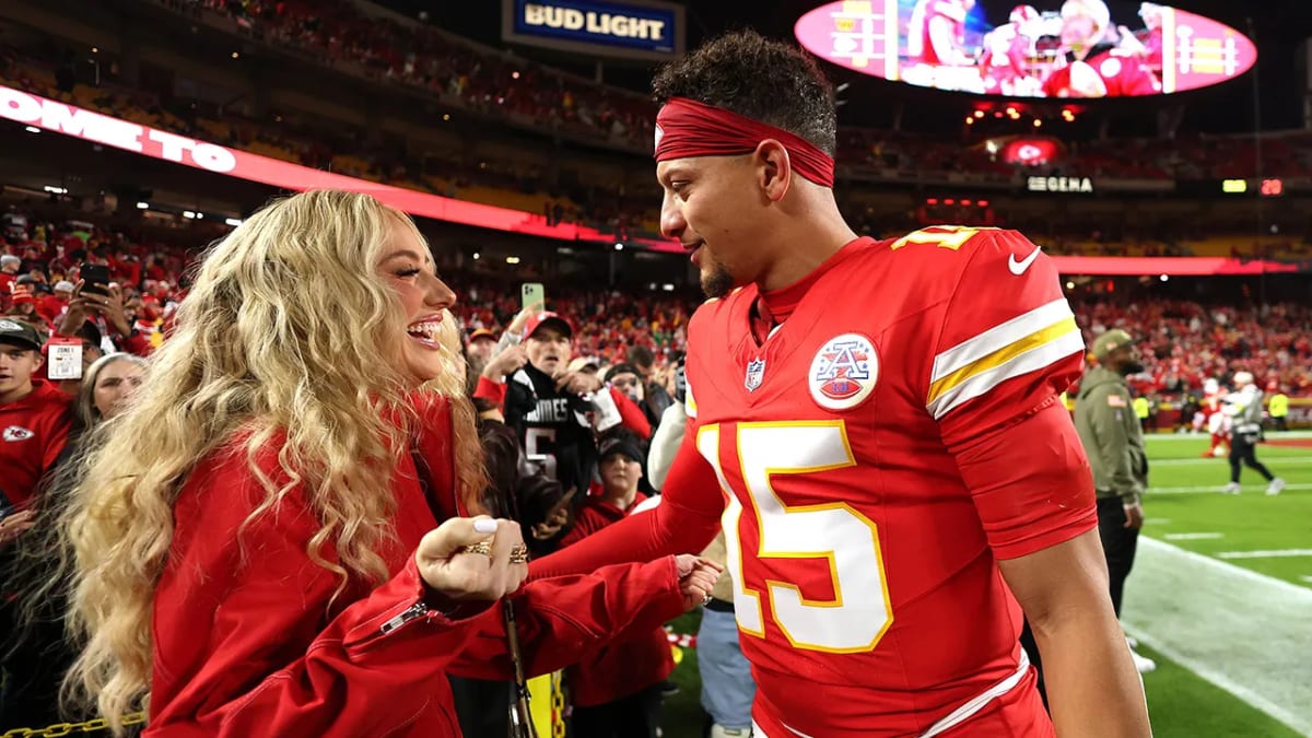 Brittany Mahomes smiling at sporting event, wearing black outfit and waving to crowd
