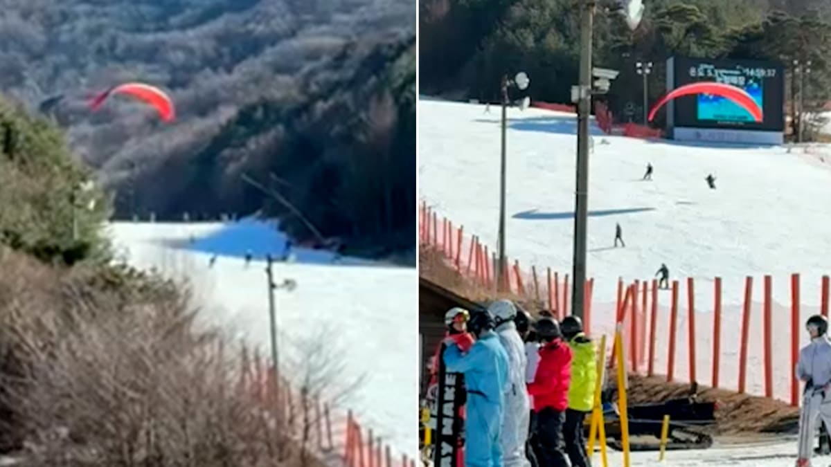 Paraglider with open canopy descending toward busy ski slope filled with skiers