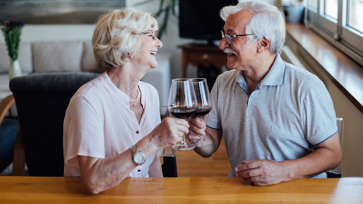 Smiling senior residents sharing drinks and conversation during happy hour at assisted living facility