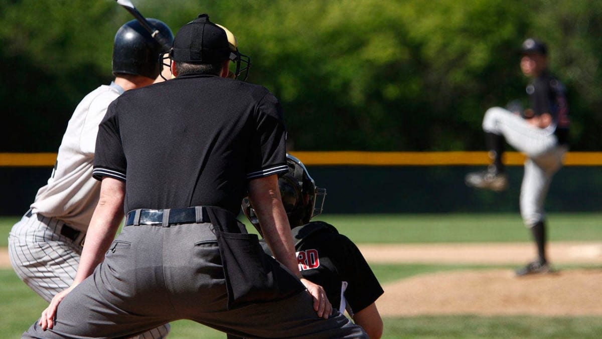 Teenage baseball umpire standing confidently on youth baseball field during game