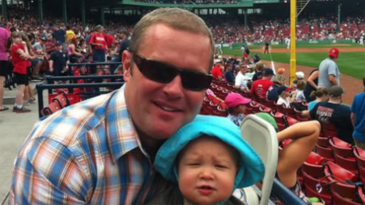 Father wearing life jacket and multi-team baseball cap at Major League Baseball stadium