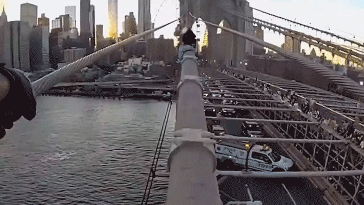 NYPD officer in uniform reaching toward woman on Brooklyn Bridge steel cables during rescue